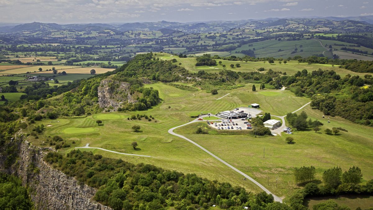 Aerial view of a clifftop golf course with fairways and greens visible, surrounded by rolling hills and farmland.